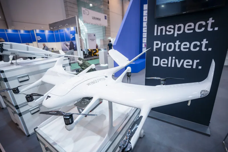 Wingcopter-Transportdrohne auf einer Transportkiste vor einem Messestand mit Werbebanner auf einer Fachmesse
