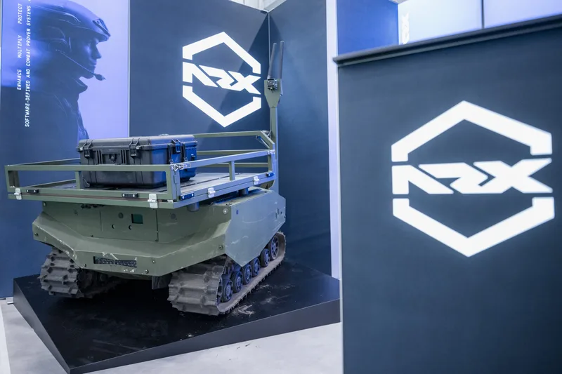 Unbemanntes Kettenfahrzeug der Gereon-Familie von ARX mit Transportbox auf einem Messestand vor Firmenlogo-Wänden