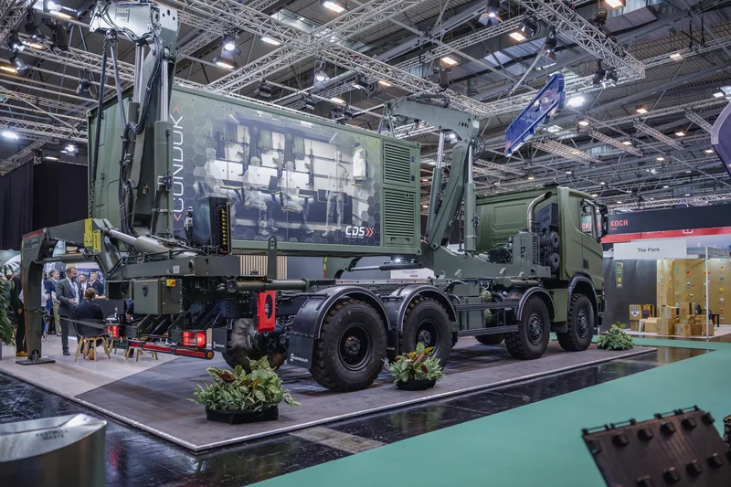 Militär-LKW mit Hammar-Seitenlader und CDS-Container mit Grafik einer Einsatzzentrale vor einem Heckler & Koch-Messestand