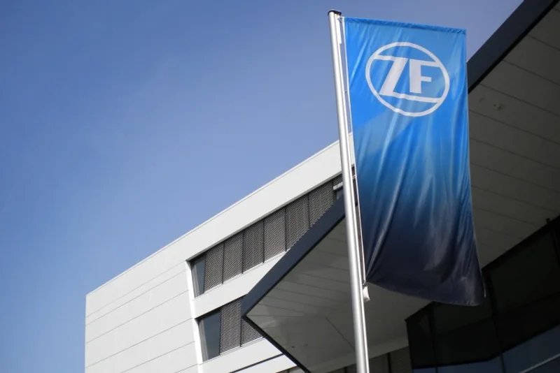Blaue Flagge mit weißem ZF-Logo weht vor einem modernen Bürogebäude unter blauem Himmel