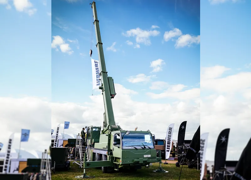 Militärischer Mobilkran Liebherr MLTB 1025-4.1 mit ausgefahrenem Teleskopausleger und Person auf der Einstiegsleiter auf einer Messe