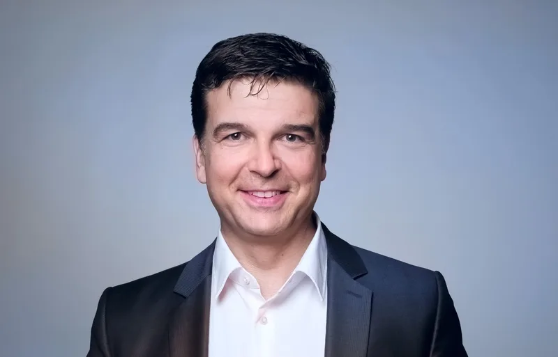 Prof. Dr. Heiko Beier, Geschäftsführer der moresophy GmbH, im dunklen Sakko und weißen Hemd vor hellblauem Hintergrund