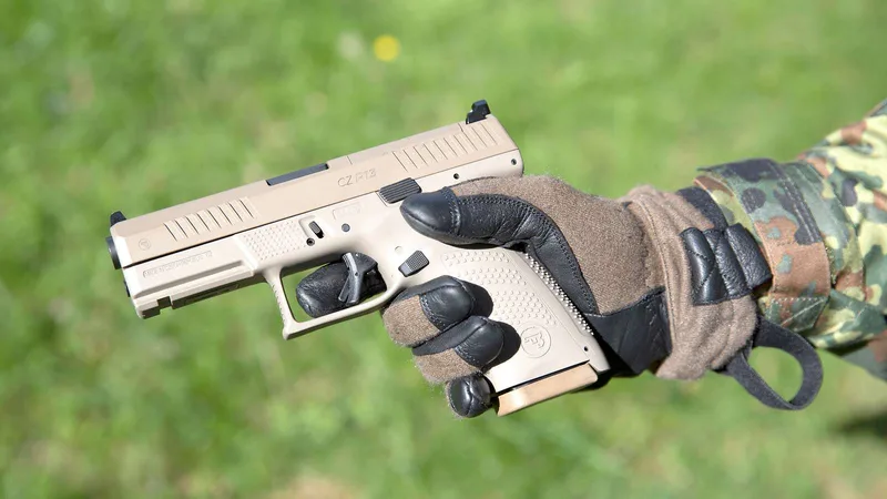 Soldat in Flecktarn-Uniform hält eine sandfarbene Pistole CZ P-10 in der behandschuhten Hand