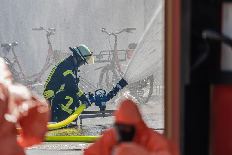 Feuerwehrmann in Schutzausrüstung bedient einen tragbaren Löschmonitor mit Wasserstrahl vor weiteren Einsatzkräften