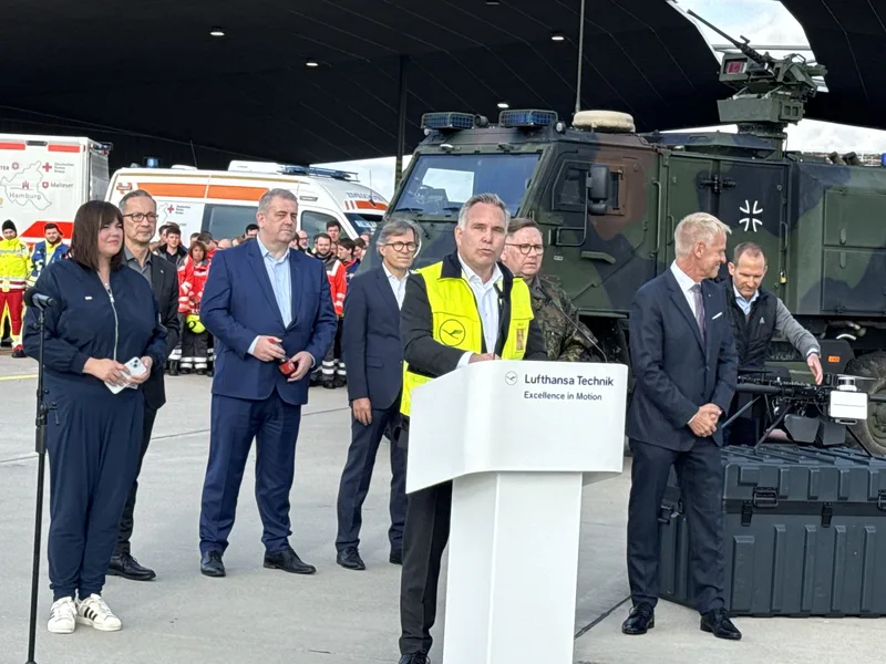 Red Storm Charlie: Sprecher am Lufthansa Technik-Rednerpult vor einem Bundeswehr-Dingo und zivilen Katastrophenschutzfahrzeugen auf einem Flugplatz