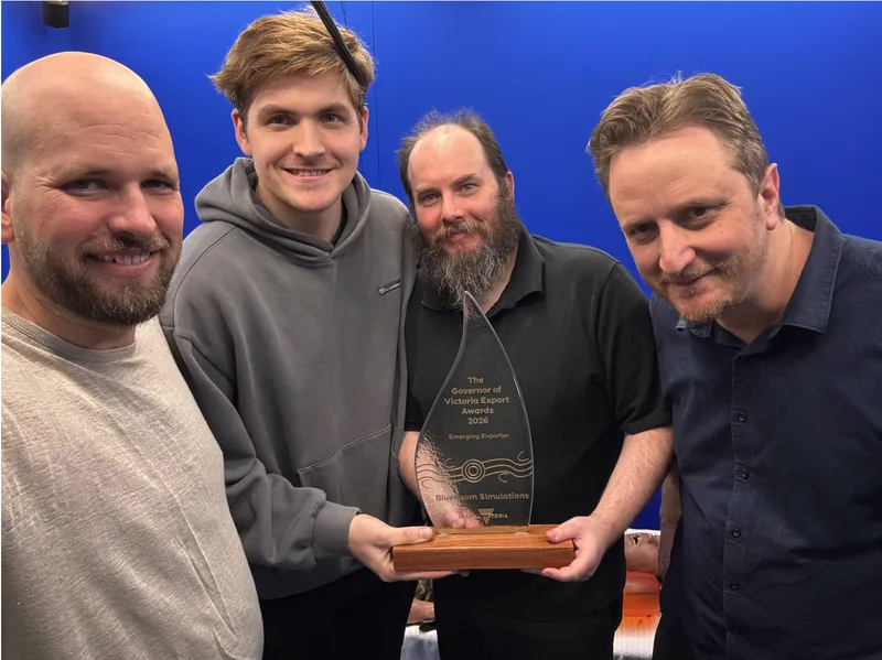 Vier Mitarbeiter von BlueRoom Simulations präsentieren eine Auszeichnung der Governor of Victoria Export Awards vor blauem Hintergrund