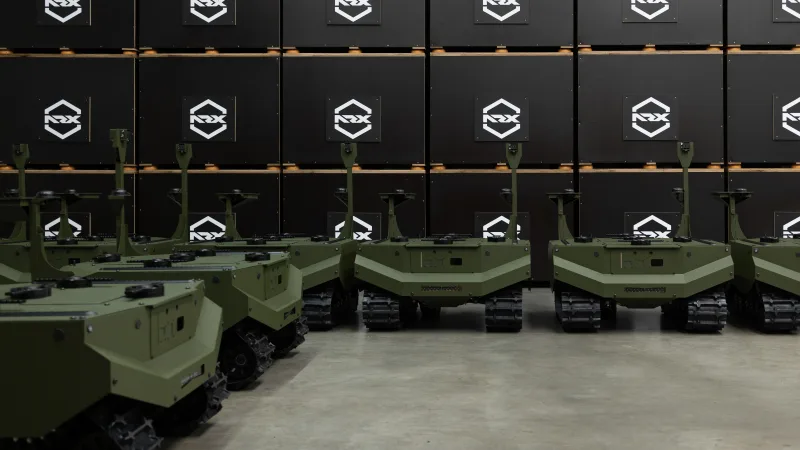 Mehrere unbemannte Kettenfahrzeuge von ARX Robotics stehen in einer Halle vor gestapelten Transportkisten des Herstellers