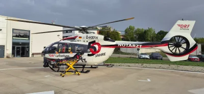 Airbus H145 Rettungshubschrauber der DRF Luftrettung mit Jubiläumslackierung und davor abgestellter Stryker-Krankentrage auf einem Landeplatz