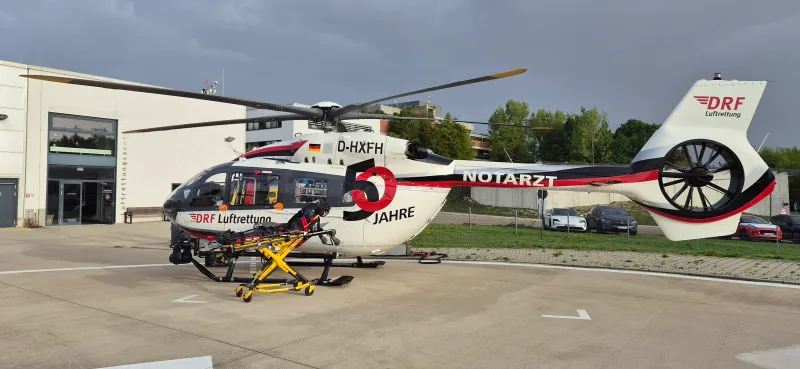 Airbus H145 Rettungshubschrauber der DRF Luftrettung mit Jubiläumslackierung und davor abgestellter Stryker-Krankentrage auf einem Landeplatz