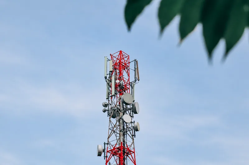 5G-Campusnetze: Rot-weißer Gittermast mit Richtfunk- und Mobilfunkantennen vor blauem Himmel mit leicht bewölktem Hintergrund