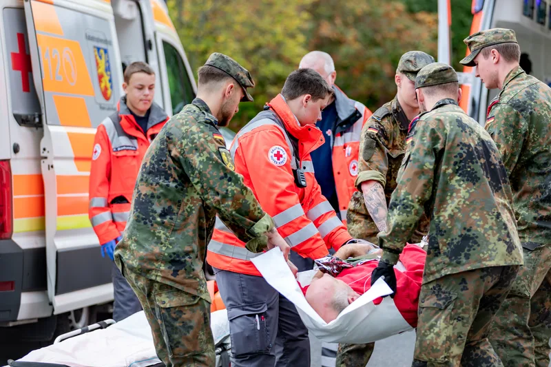 Soldaten der Bundeswehr und Einsatzkräfte des Deutschen Roten Kreuzes verlegen gemeinsam einen Patienten in einen Rettungswagen