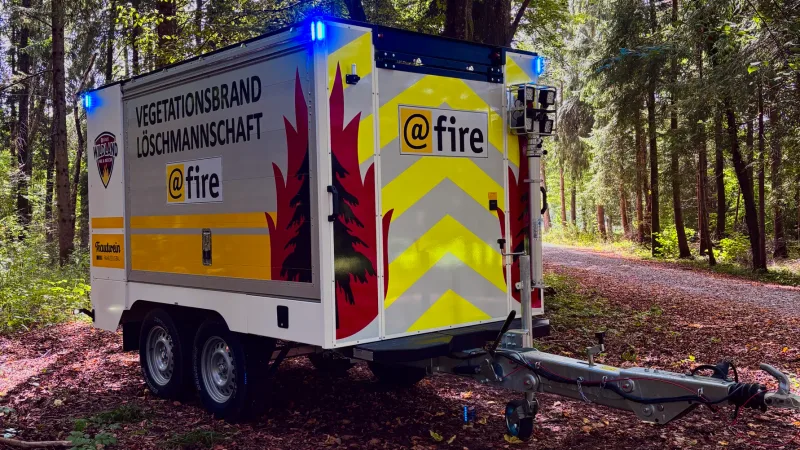 Hilfe beim Vegetationsbrand: Zweiachsiger Trautwein-Einsatzanhänger von @fire mit Lichtmast und Warnbeklebung zur Vegetationsbrandbekämpfung auf einem Waldweg
