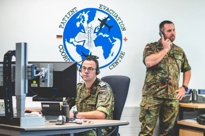 Zwei Bundeswehr-Soldaten in Flecktarn arbeiten im Patient Evacuation Coordination Centre an Computer und Telefon