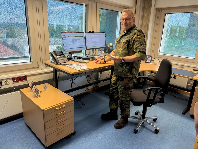 Offizier der Bundeswehr und Gruppenleiter im BAAINBw an einem höhenverstellbaren Schreibtisch mit Arbeitsübersichten auf Bildschirmen