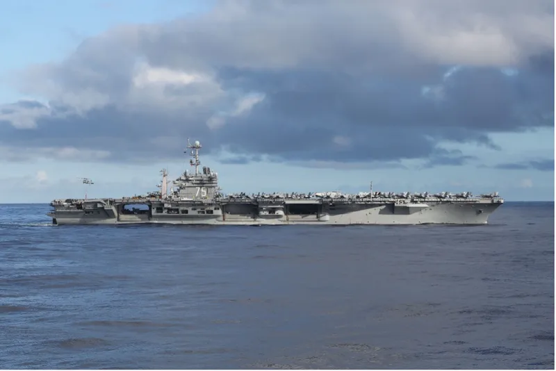 Flugzeugträger USS Harry S. Truman der US Navy mit abgestellten Flugzeugen auf dem Deck und einem Hubschrauber im Flug