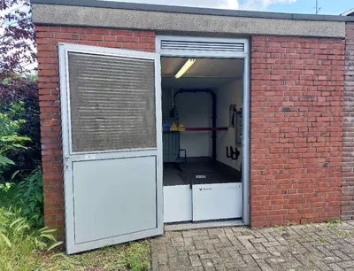 Starkregen: Geöffnete Transformatorenstation mit Hochwasserschutzbarriere am Eingang sowie sichtbaren elektrischen Anlagen und Warnhinweisen