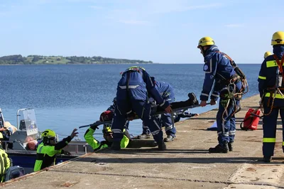 Einsatzkräfte des THW bergen bei einer Rettungsübung eine Person auf einer Trage von einem Boot auf eine Kaimauer
