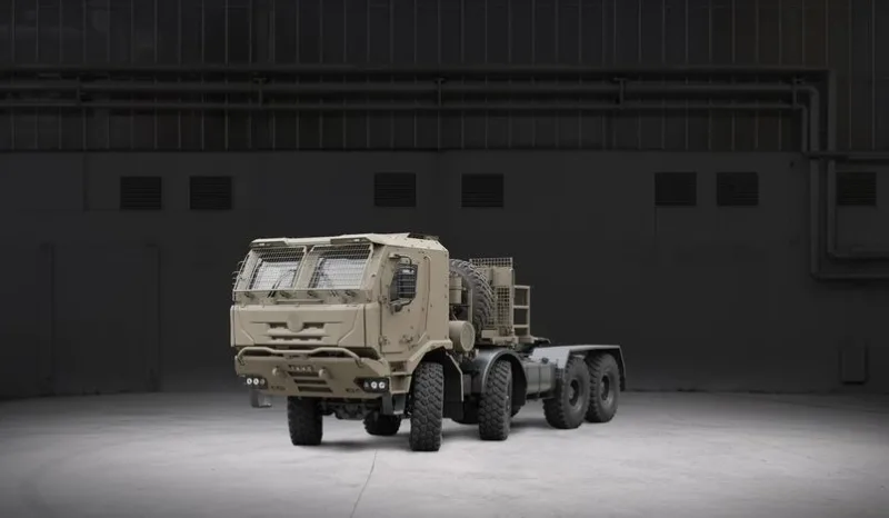 Sandfarbene militärische Sattelzugmaschine Tatra Force 8x8 mit geschützter Fahrerkabine und Schutzgittern in einer Industriehalle