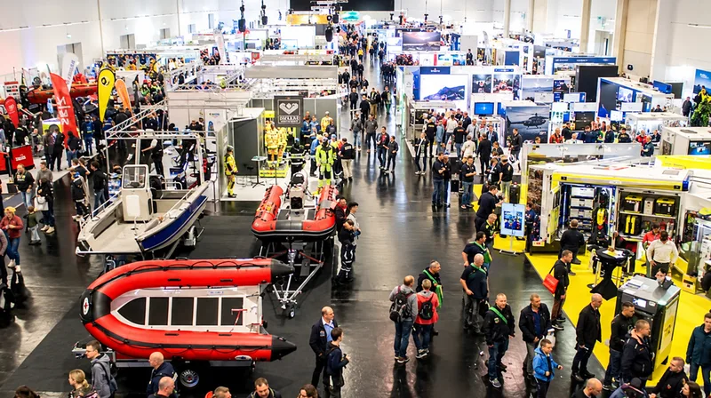 Florian: Besucher in einer Messehalle für Katastrophenschutz zwischen Rettungsbooten, Einsatzfahrzeugen und Ständen mit Schutzausrüstung