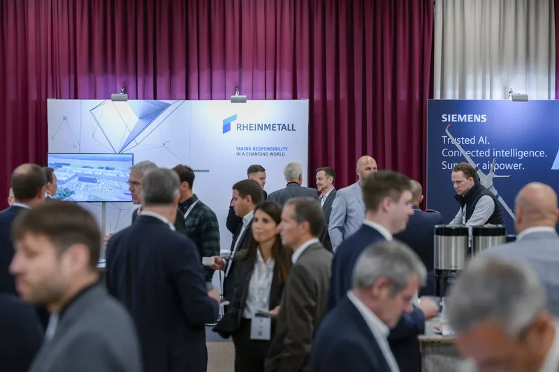 Fachbesucher im Gespräch vor den Messeständen von Rheinmetall und Siemens auf einer Rüstungs- und Technologiefachmesse