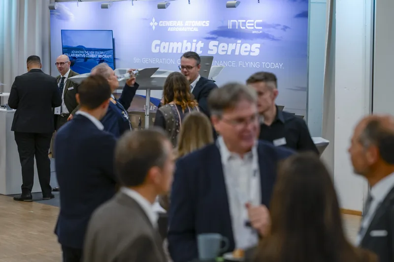 Fachbesucher und Militärangehörige am Messestand von General Atomics Aeronautical und Intec Group mit Gambit-Drohnenmodell