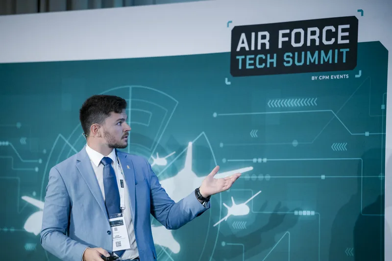 Lukas Kaltenbach referiert auf dem Air Force Tech Summit von CPM Events vor einer Grafik mit Silhouetten von Luftfahrzeugen