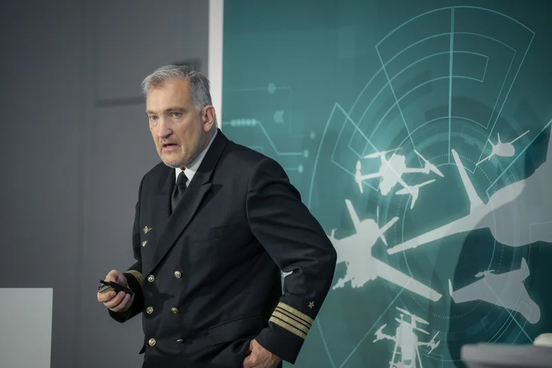 Kapitän zur See der Deutschen Marine hält Vortrag vor einer Grafikwand mit unbemannten Flugsystemen und Radarsignaturen