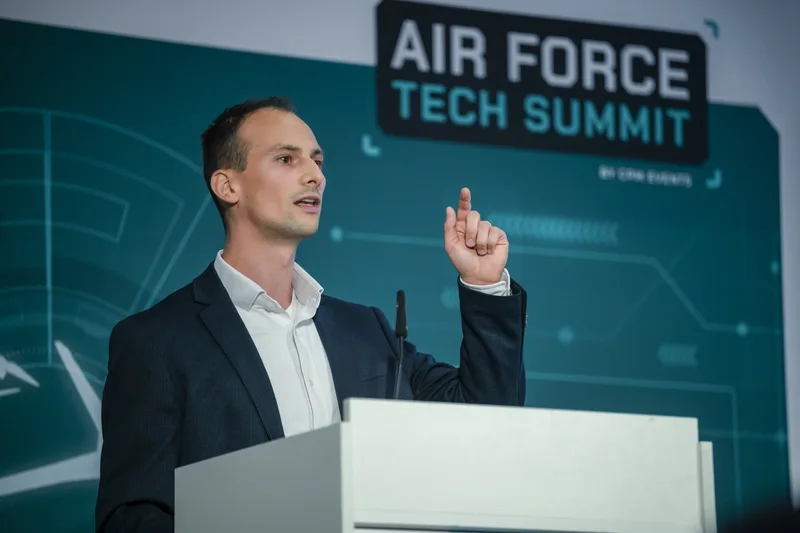 Referent spricht an einem Rednerpult während des Air Force Tech Summit von cpm events vor einer grafisch gestalteten Kulisse