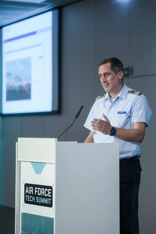Luftwaffenoffizier in Dienstuniform spricht am Rednerpult während des Air Force Tech Summit vor einer Präsentationsleinwand