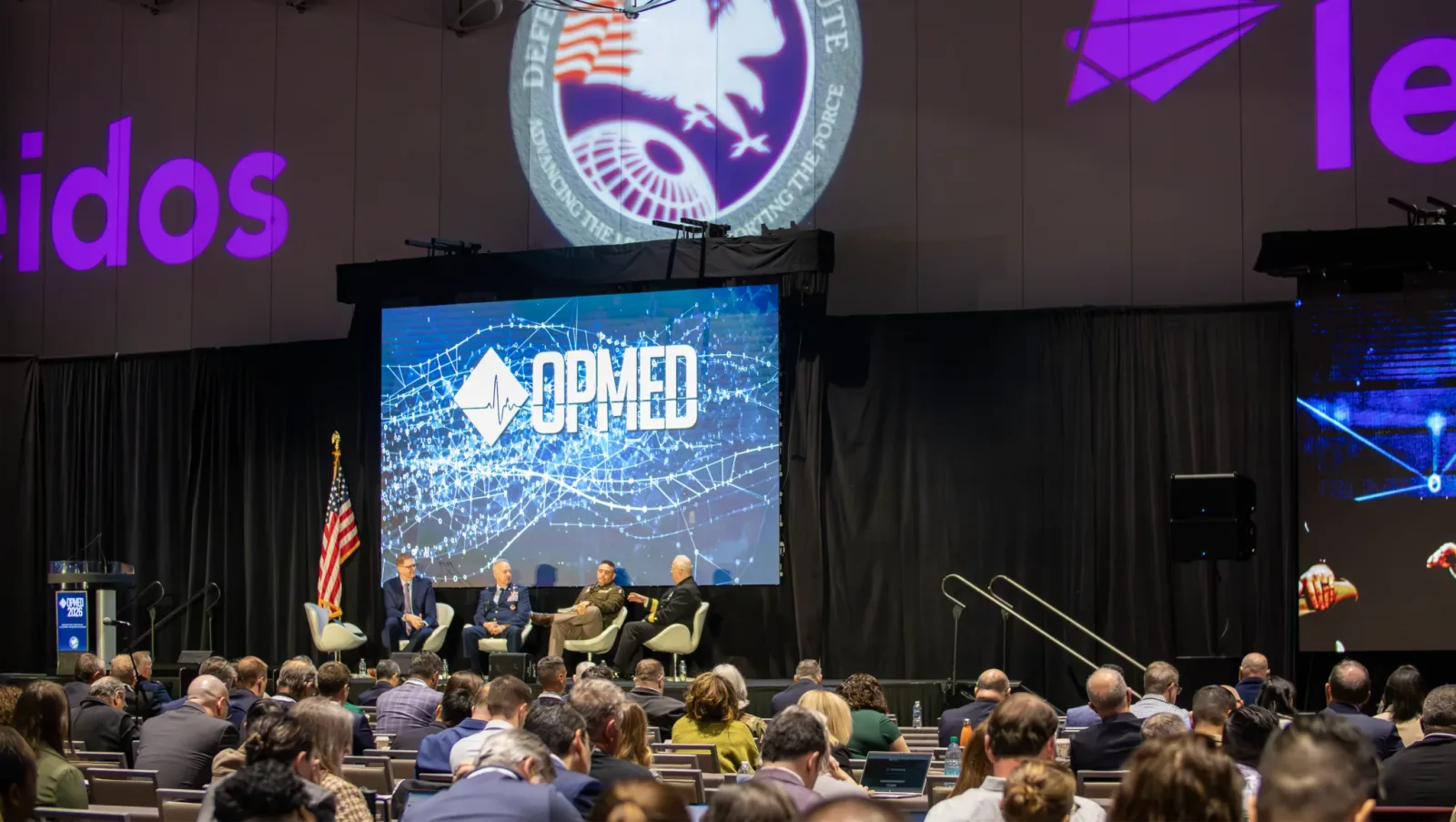 US-Offiziere bei einer Podiumsdiskussion auf der OPMED-Konferenz vor Bannern der US-Streitkräfte und des Unternehmens Leidos