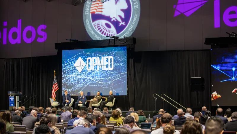 US-Offiziere bei einer Podiumsdiskussion auf der OPMED-Konferenz vor Bannern der US-Streitkräfte und des Unternehmens Leidos