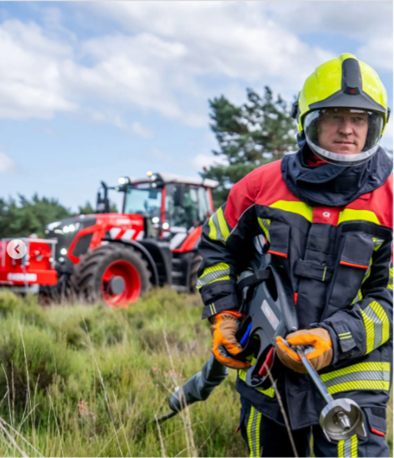 Feuerwehrmann in Schutzkleidung mit Löschlanze bei der Vegetationsbrandbekämpfung neben einem Traktor mit Fronttank im Gelände