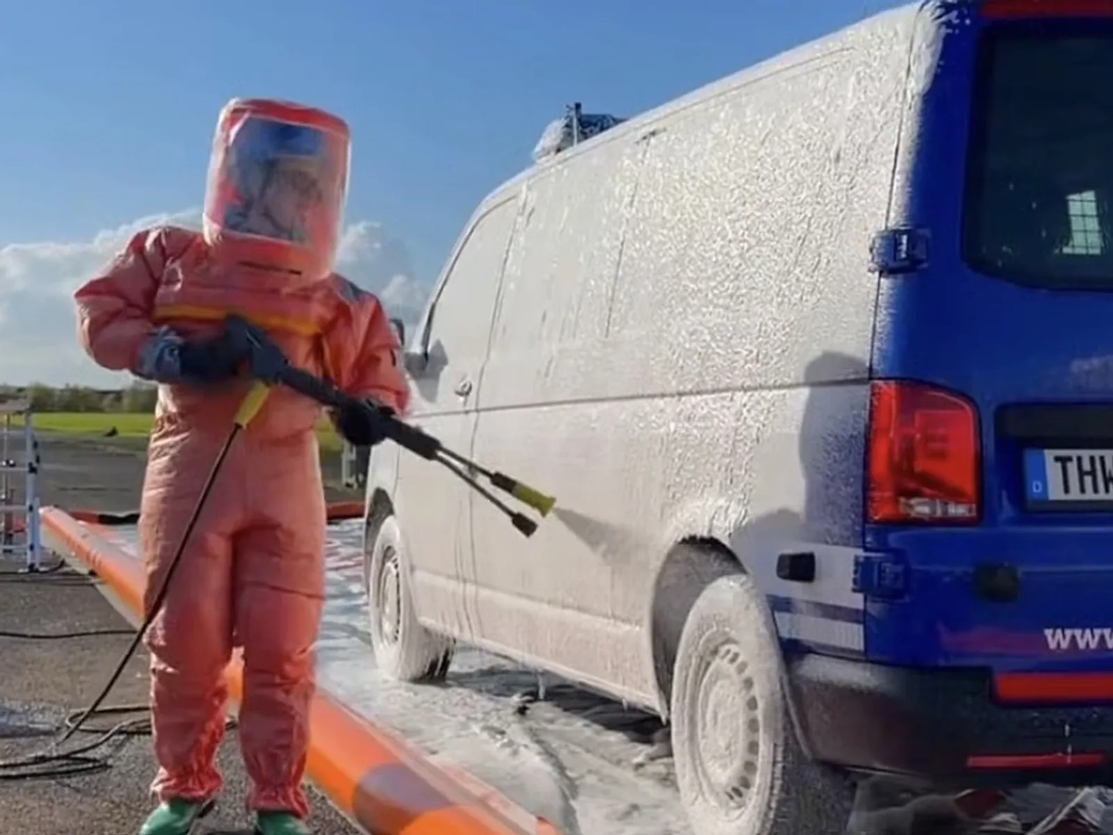 Einsatzkraft in Chemikalienschutzanzug dekontaminiert einen blauen THW-VW-Transporter mit Schaum in einer mobilen Wanne