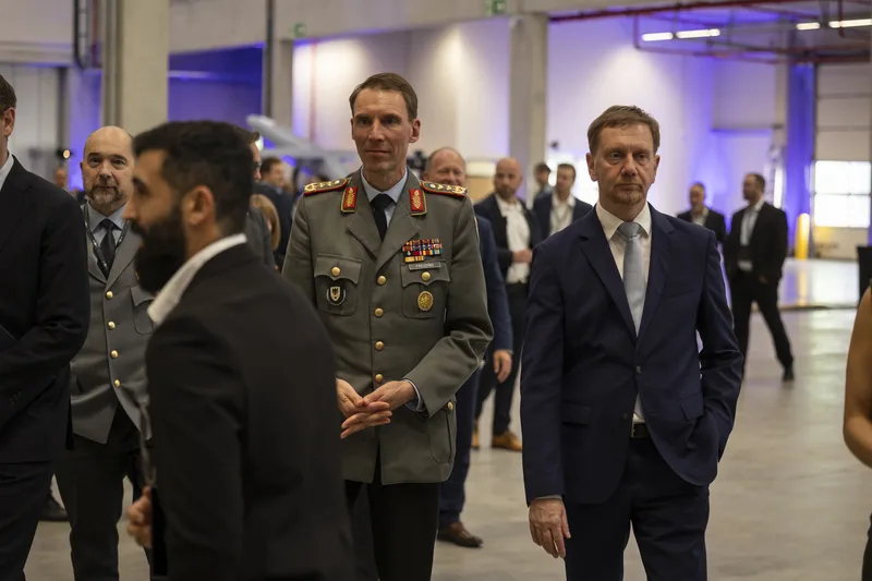 Generalmajor Christian Freuding und Ministerpräsident Michael Kretschmer bei einem Rundgang in einer Industriehalle mit weiteren Gästen