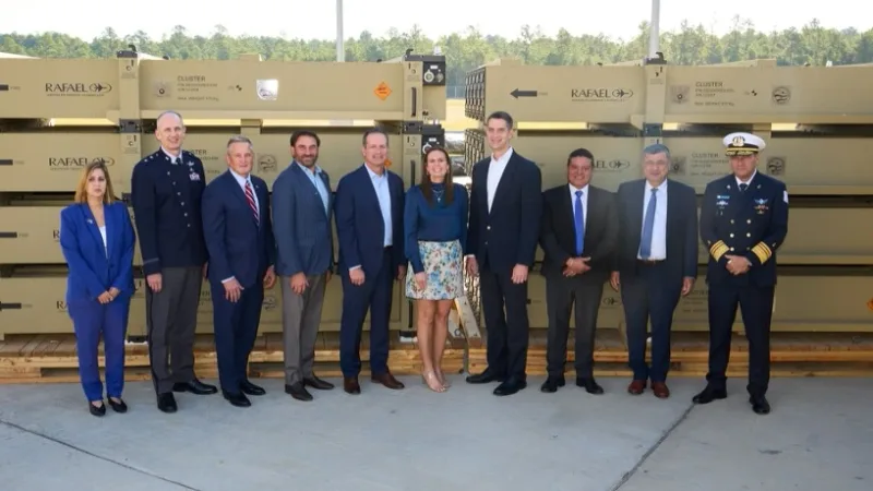 Militärische und zivile Delegation vor gestapelten Transportbehältern von Rafael Advanced Defense Systems im Freien