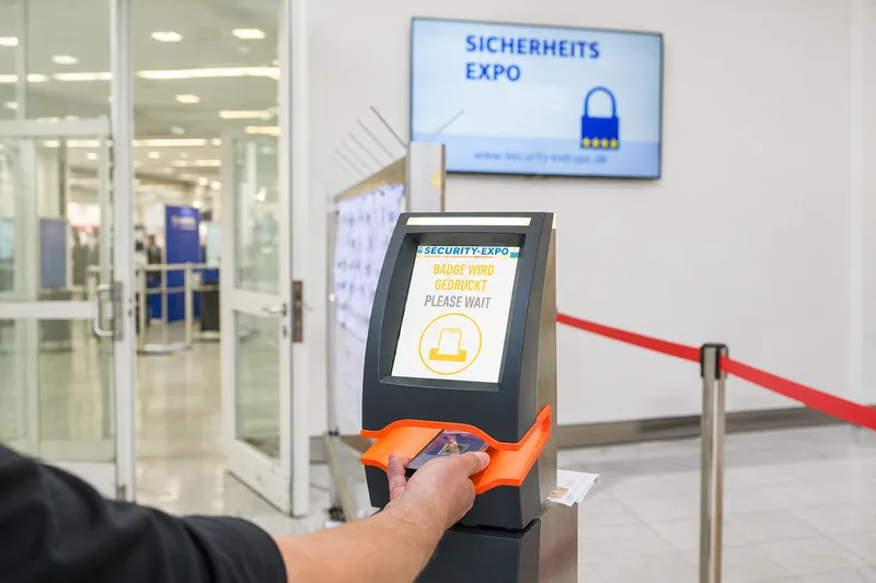 Besucher scannt Mobiltelefon an einem Registrierungsterminal der SicherheitsExpo zur automatischen Ausgabe eines Besucherausweises