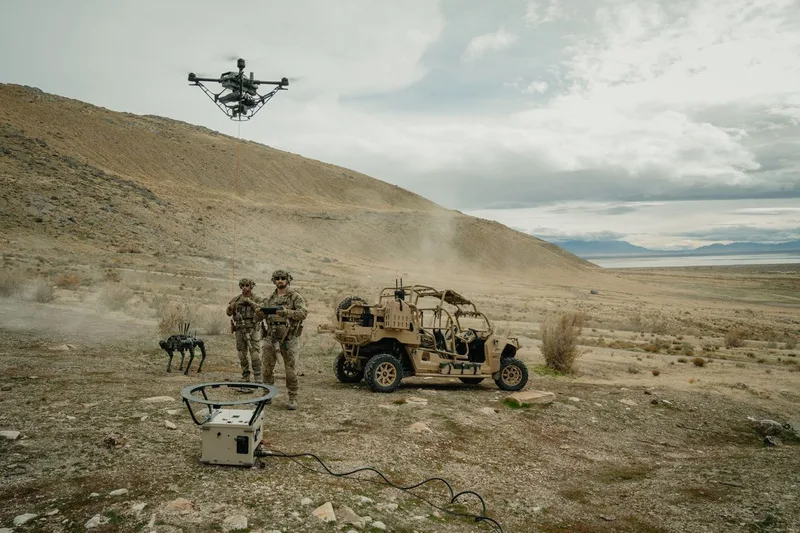 Zwei Soldaten testen in offenem Gelände eine Fesseldrohne, einen vierbeinigen Laufroboter und ein Polaris MRZR Geländefahrzeug