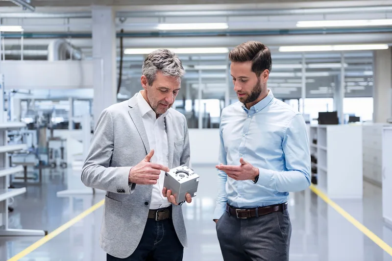 Zwei Fachkräfte begutachten in einer Industriehalle ein präzisionsgefrästes Metallbauteil für die Verteidigungstechnik