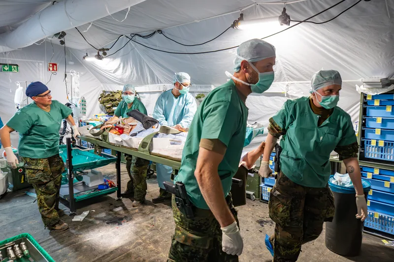 Sanitätspersonal der Bundeswehr transportiert einen Patienten auf einer Krankentrage in einem mobilen Role-2-Sanitätszelt
