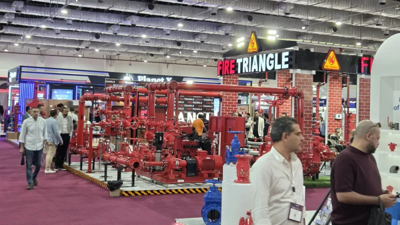 Besucher am Messestand von Fire Triangle mit industriellen Pumpensystemen, roten Rohrleitungen und Ventilen für den Brandschutz