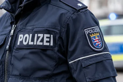 Frankfurt: Polizeibeamter der hessischen Polizei in Einsatzbekleidung mit Landeswappen vor einem Einsatzfahrzeug mit Blaulicht