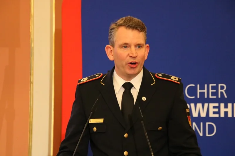 Dr. Christoph Weltecke in Feuerwehruniform spricht an einem Rednerpult vor dem Logo des Deutschen Feuerwehrverbandes
