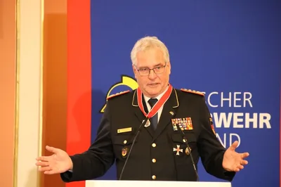 Karl-Heinz Banse, Präsident des Deutschen Feuerwehrverbandes, spricht in Dienstuniform an einem Rednerpult vor einem DFV-Logo