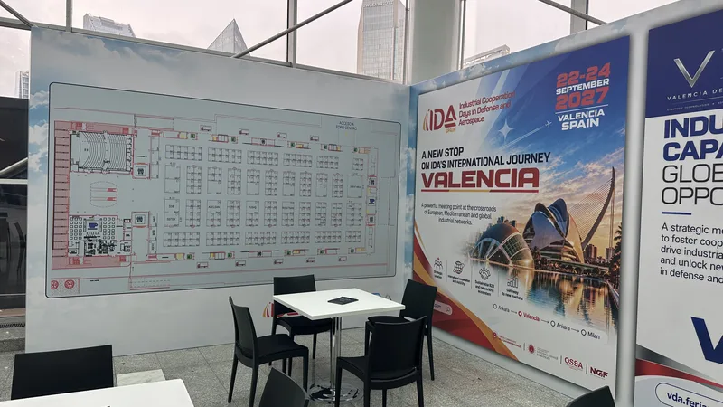 Besprechungsbereich mit Tisch und Stühlen vor Hallenplänen und Werbebannern auf einer Verteidigungs- und Luftfahrtmesse in Valencia