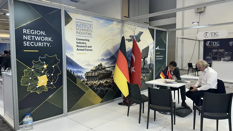 Messestand des Mitteldeutschen Instituts für Sicherheitsindustrie mit zwei Personen im Gespräch vor wehrtechnischen Grafiken