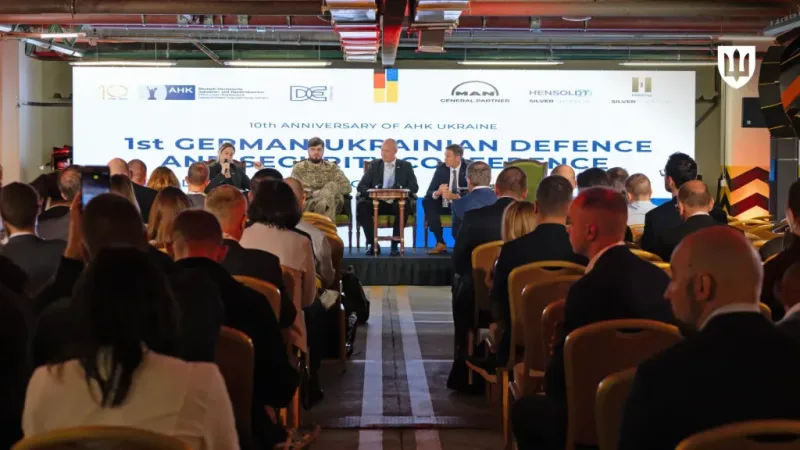 Podiumsdiskussion auf der deutsch-ukrainischen Verteidigungskonferenz mit Vertretern vor einer Leinwand mit Logos von MAN, Hensoldt und Helsing