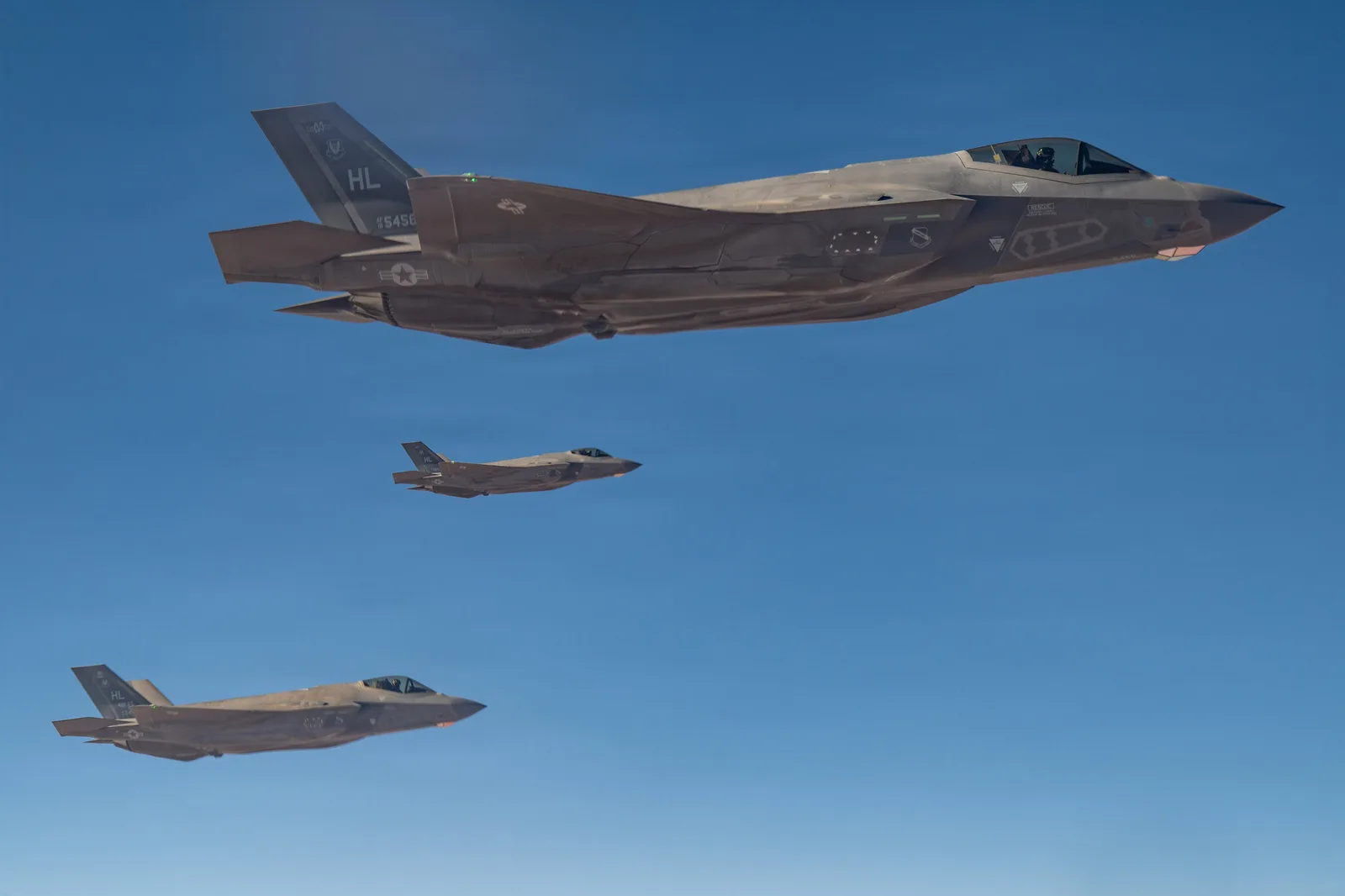 Drei Lockheed Martin F-35 Lightning II der US Air Force mit HL-Leitwerkskennung fliegen in Formation vor klarem Himmel