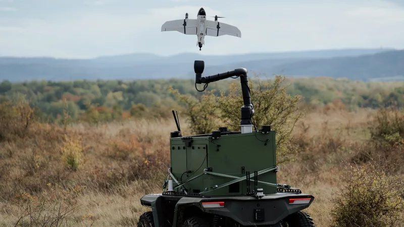 Senkrechtstartfähige Drohne von Quantum Systems über einem unbemannten Landfahrzeug mit automatisiertem Fangarm im Gelände