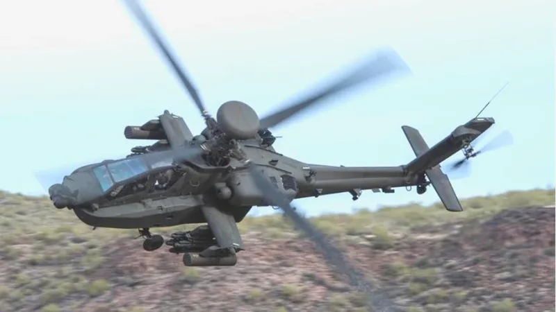 Boeing AH-64 Apache Kampfhubschrauber mit Mastradar und Außenlasten im Flug über hügeligem Gelände