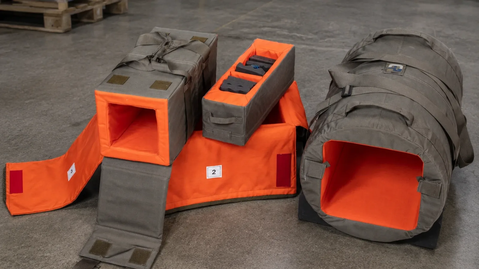 GARANT: Olivgraue textile Schutz- und Transporthüllen mit signalorangefarbenem Innenfutter und Haltegurten lagern in einer Halle